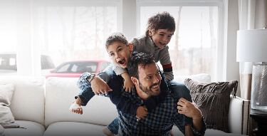 Father and two kids playing with a car in the background